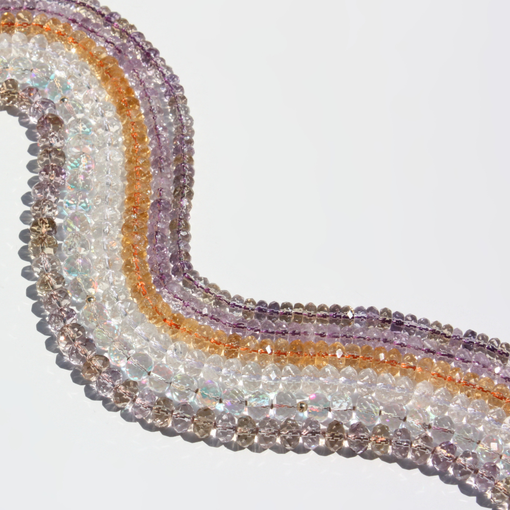 Multiple faceted beaded necklace lined up together laid flat on a white background. 