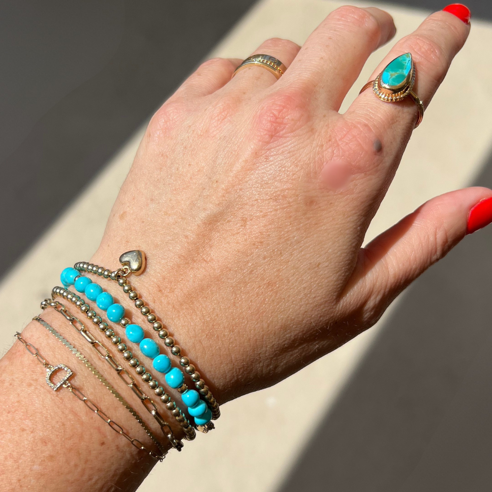 Model wearing a 14k solid gold sleeping beauty turquoise bracelet layered with fine gold bracelets.