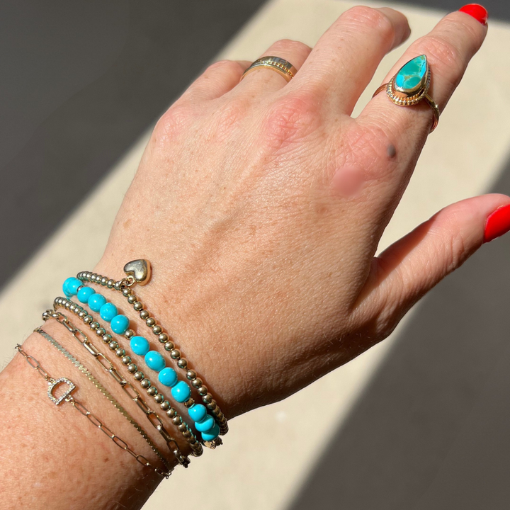 Model wearing a 14k solid gold sleeping beauty turquoise bracelet layered with fine gold bracelets.