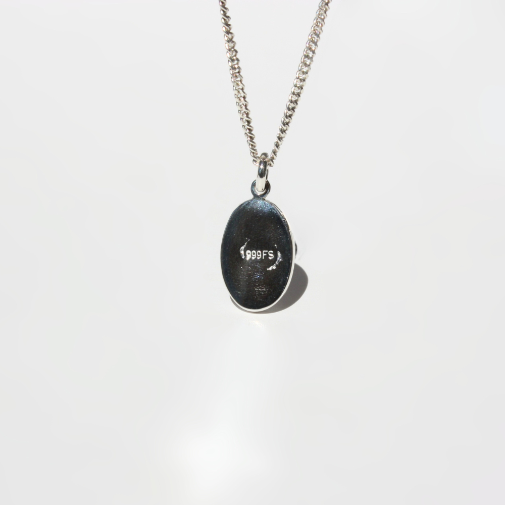 A fine silver chain necklace with an oval pendant showing the backside of the pendant with quality mark.