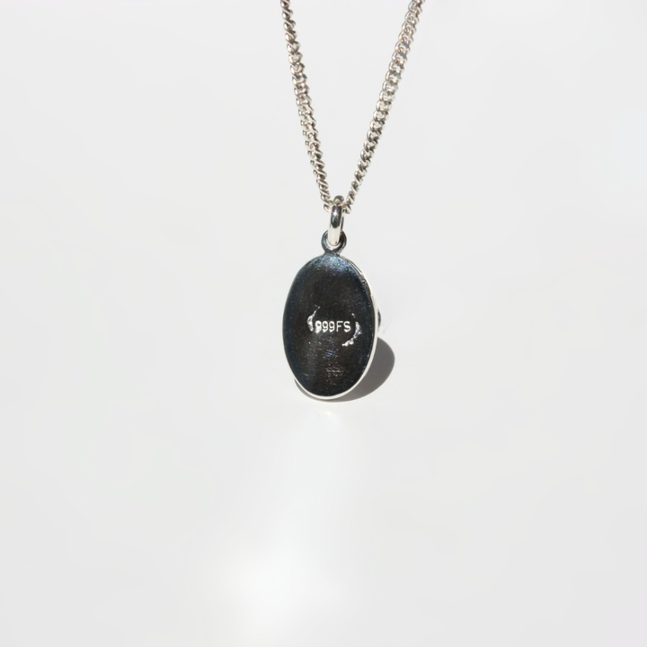 A fine silver chain necklace with an oval pendant showing the backside of the pendant with quality mark.