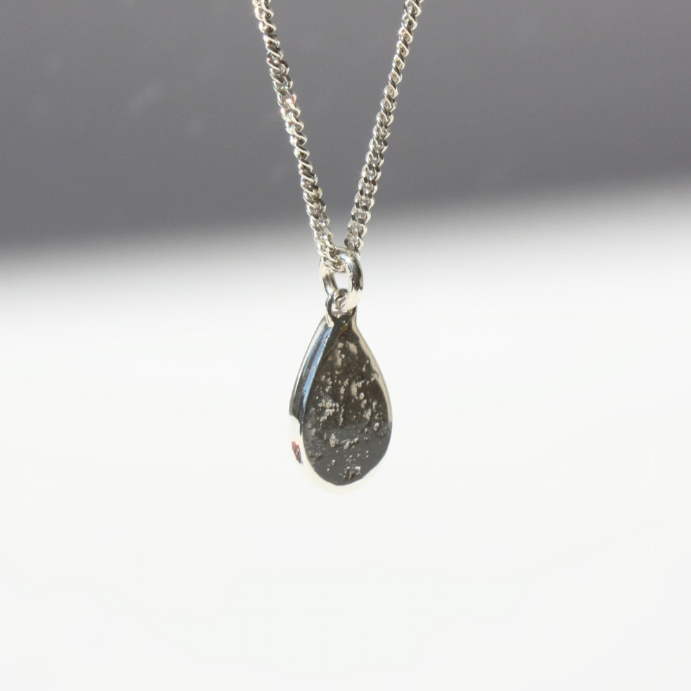 "Detail view of organic sand cast fine silver texture framing a cast in place pear center stone."