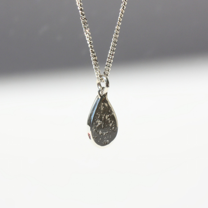 "Detail view of organic sand cast fine silver texture framing a cast in place pear center stone."