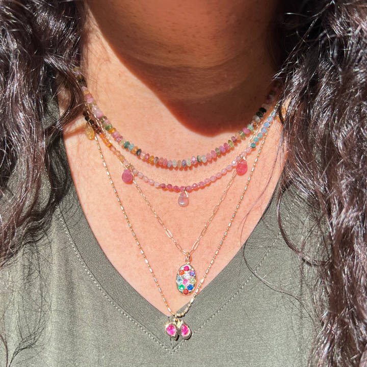 "Model wearing a 14k gold oval coin multi gemstone rainbow pendant necklace layered with 14k gold chains."