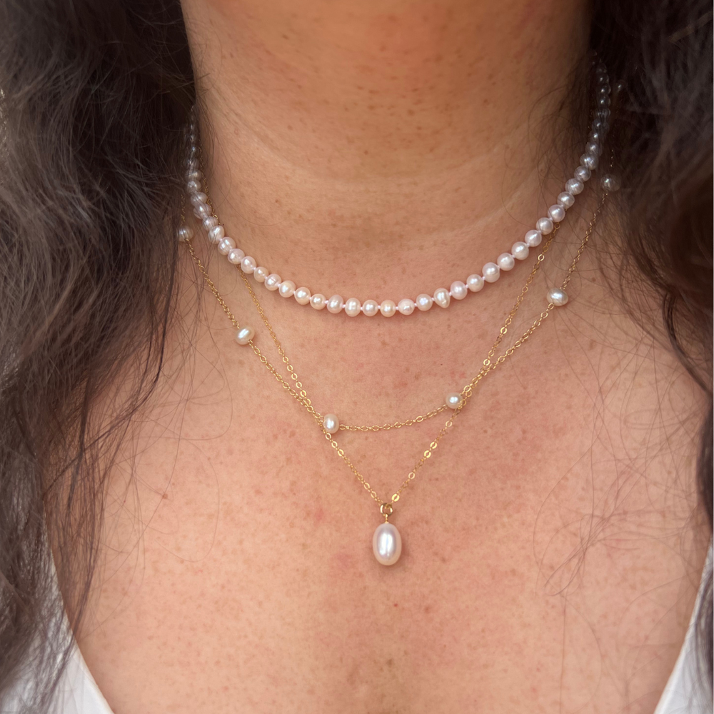 Model wearing a 14k gold pearl drop station necklace layered with fine gold chains.