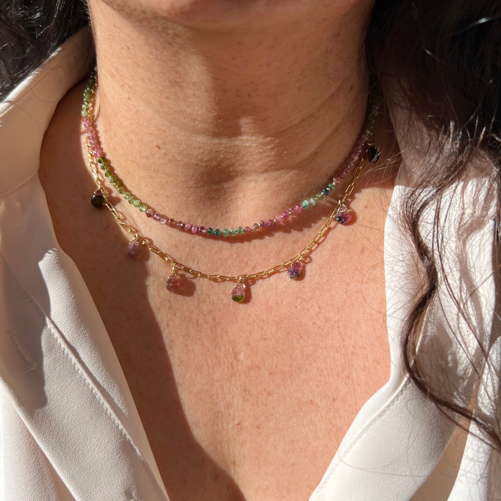 "Model wearing a watermelon tourmaline teardrop paperclip necklace layered with gold coin pendants."