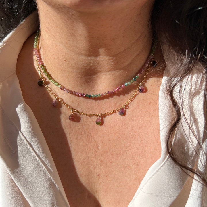 "Model wearing a watermelon tourmaline teardrop paperclip necklace layered with gold coin pendants."
