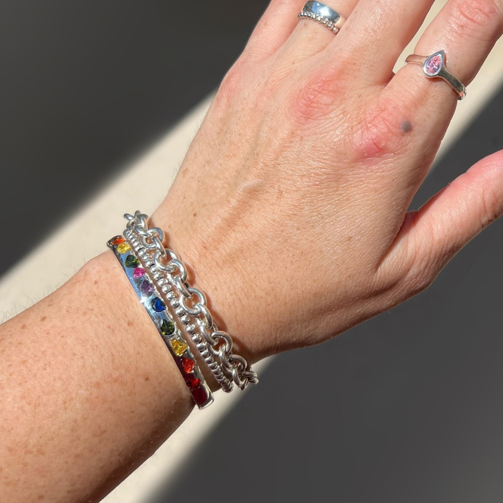 "Model wearing a sterling silver sand cast rainbow gemstone cuff bracelet stacked with silver bangles."