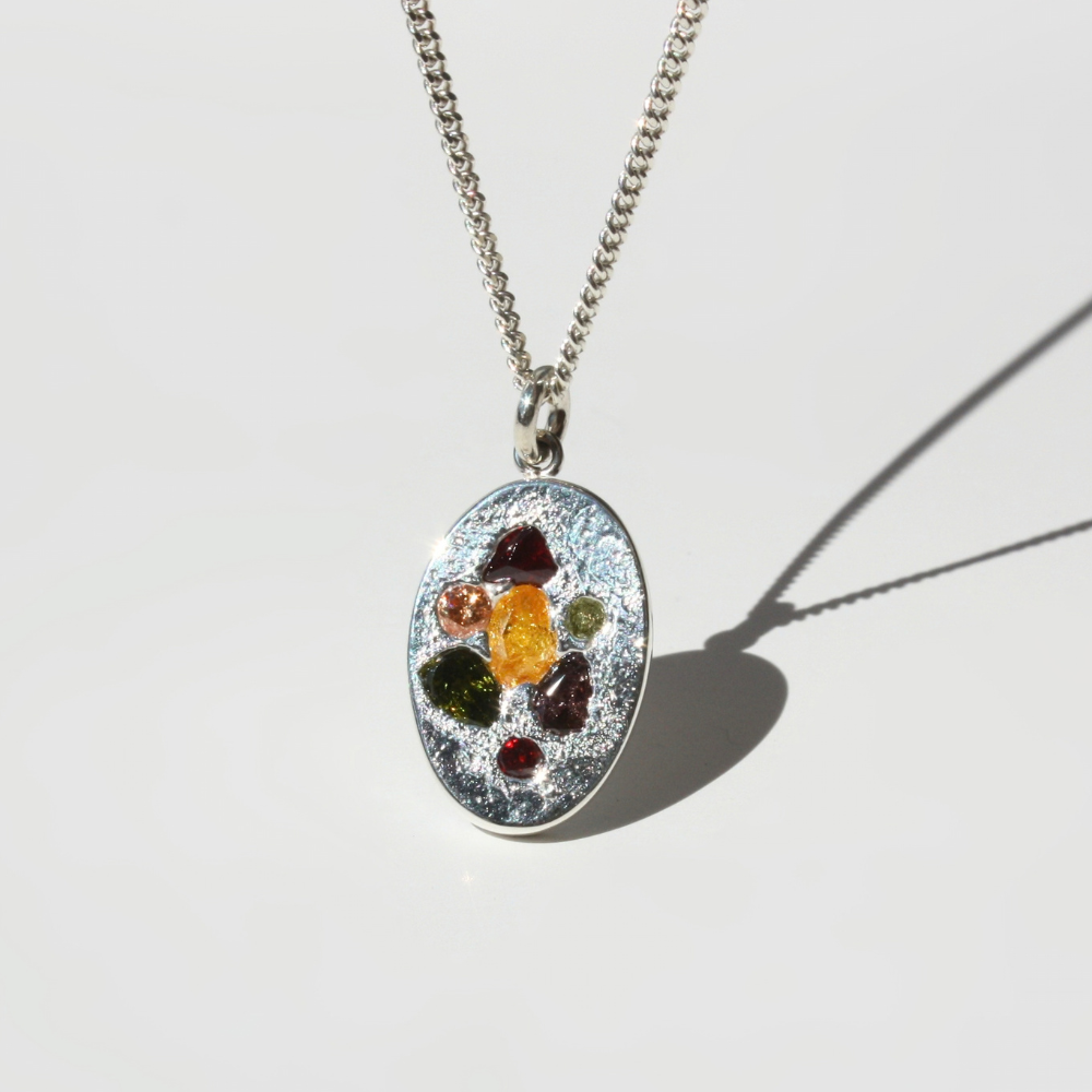 "Detail view of organic sand cast fine silver coin texture with 7 cast in place multi-color gemstones."
