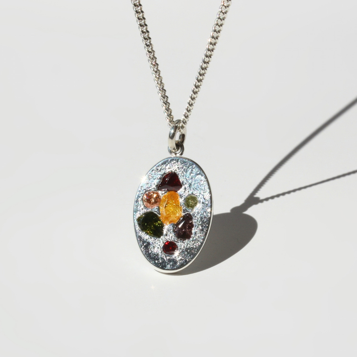 "Detail view of organic sand cast fine silver coin texture with 7 cast in place multi-color gemstones."