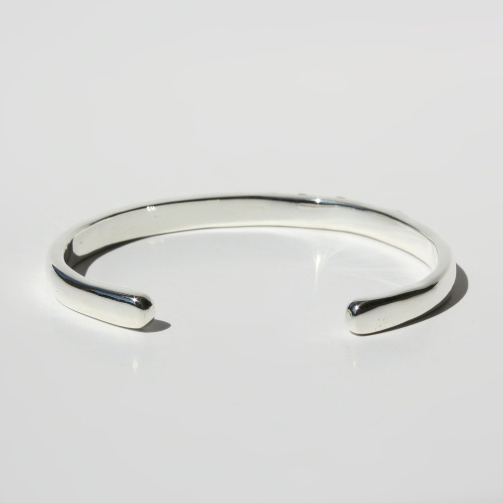 "Detail view of organic sand cast sterling silver cuff texture with cast in place lab grown fireable rainbow gemstones."