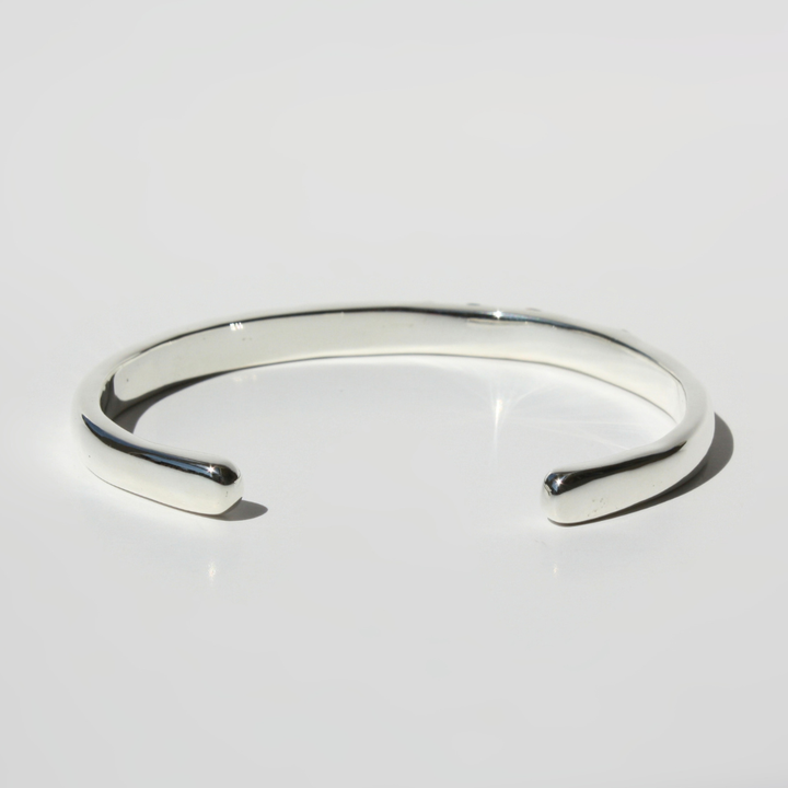 "Detail view of organic sand cast sterling silver cuff texture with cast in place lab grown fireable rainbow gemstones."