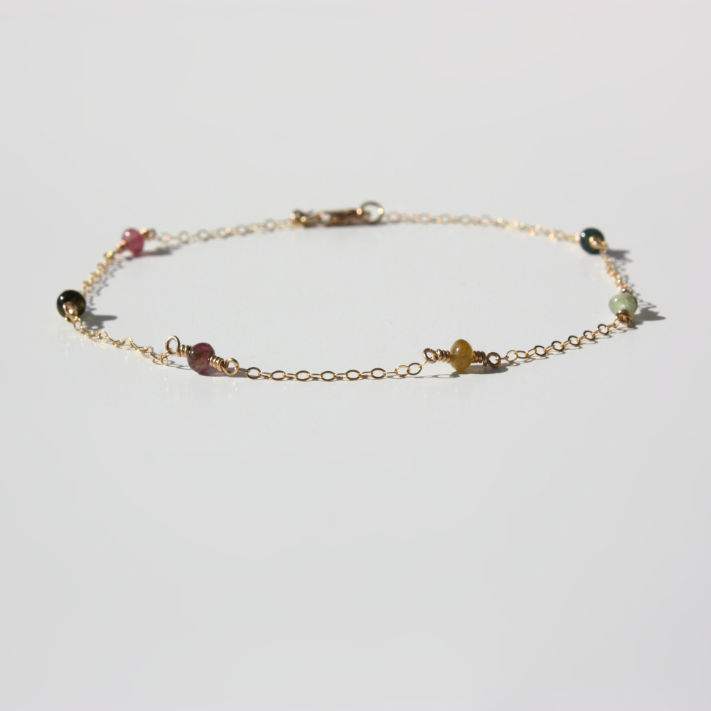 Delicate gold bracelet with small multicolored beads laid flat on a white background