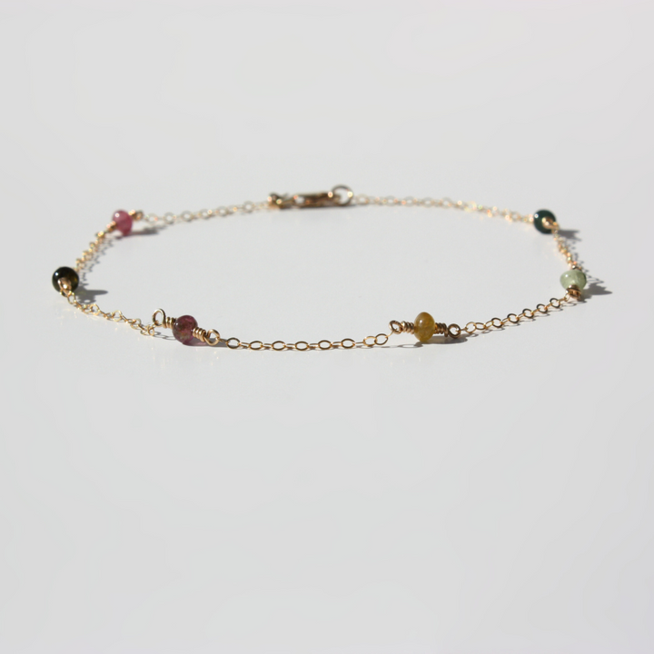 Delicate gold bracelet with small multicolored beads laid flat on a white background