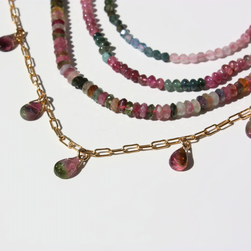 "Detail view of faceted watermelon tourmaline teardrop gemstone drops along a gold paperclip chain."