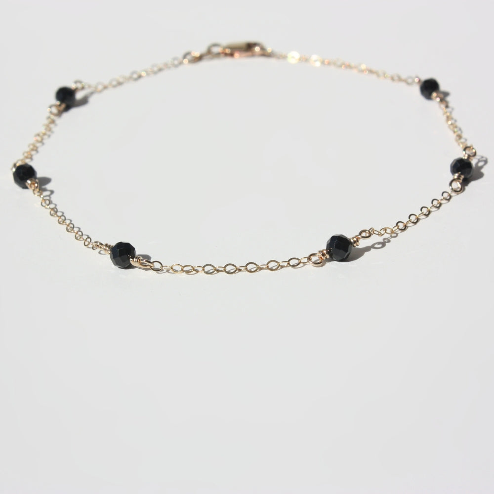 A gold-filled anklet featuring black gemstones laid flat on a white background.