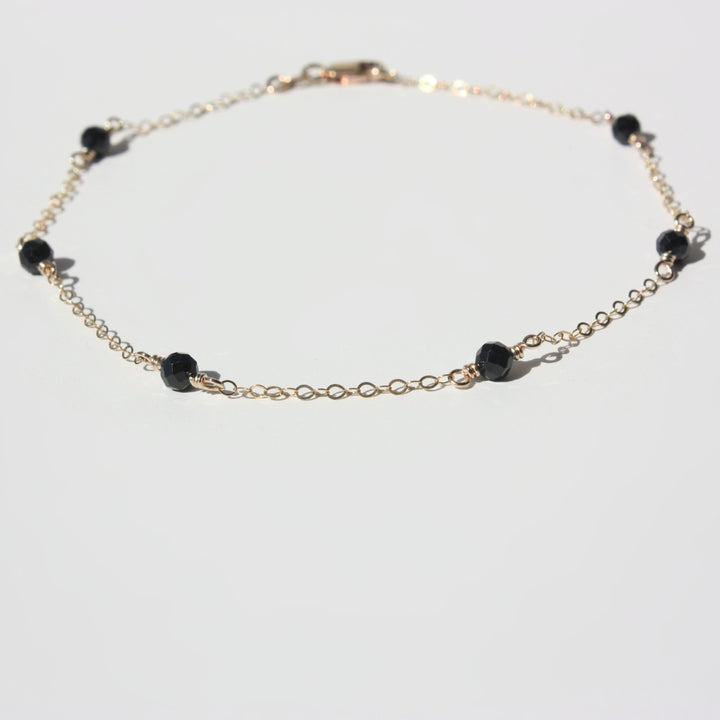 A gold-filled anklet featuring black gemstones laid flat on a white background.